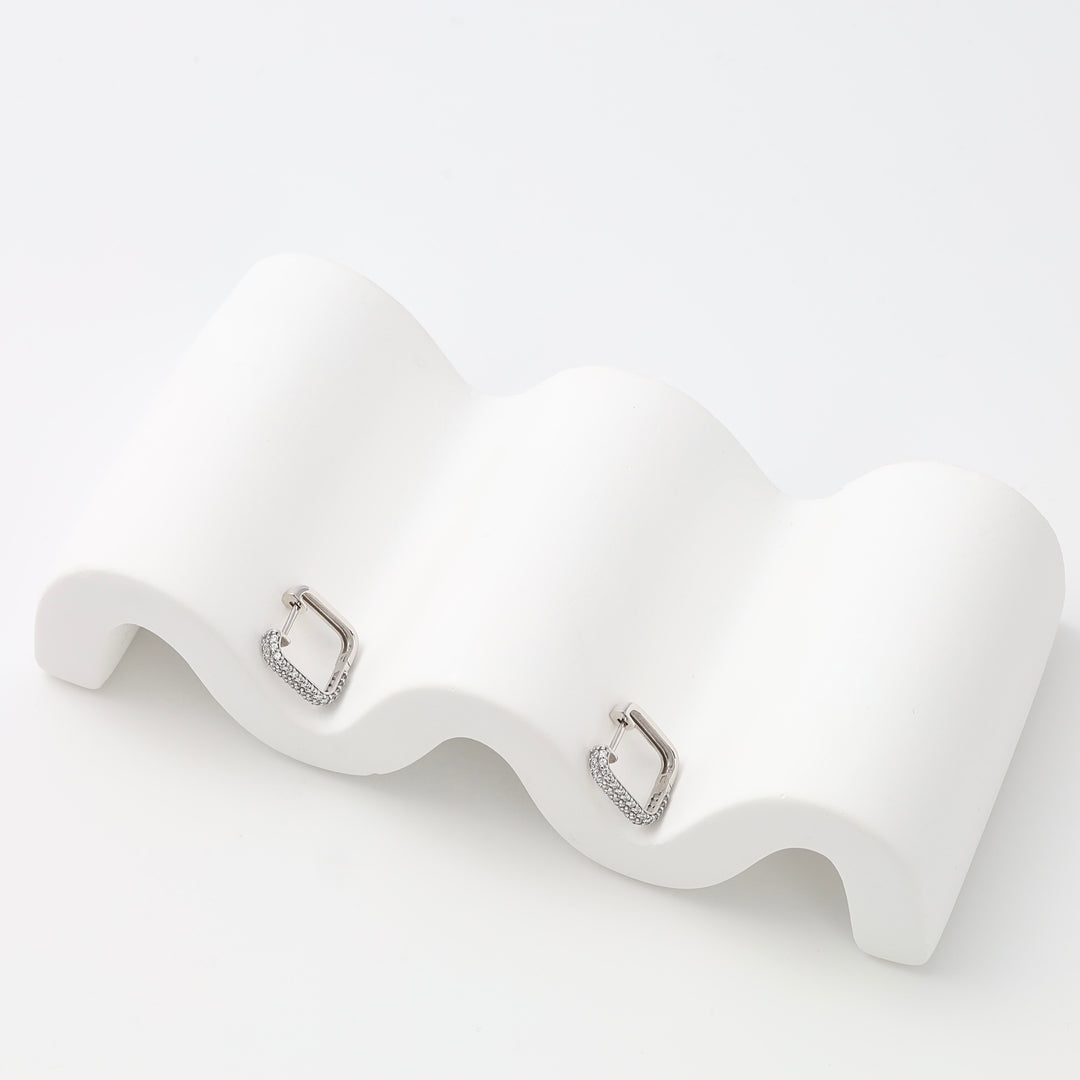 Sterling silver geometric huggie hoop earrings with pavé detail on a white display, Ukrainian Jewelry, modern minimalist earrings.