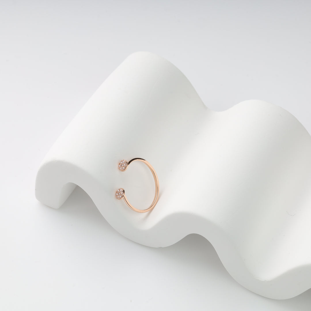 Rose gold adjustable ring with crystal-studded ball ends on white wavy display.