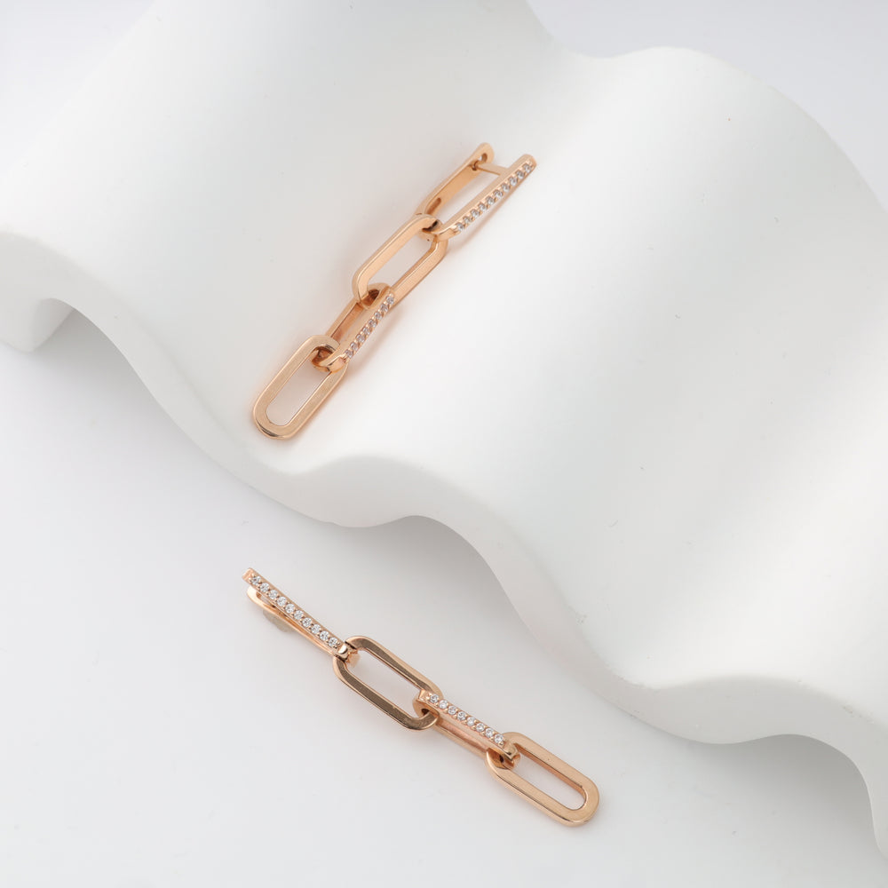 Gold link chain earrings on a white wavy surface.