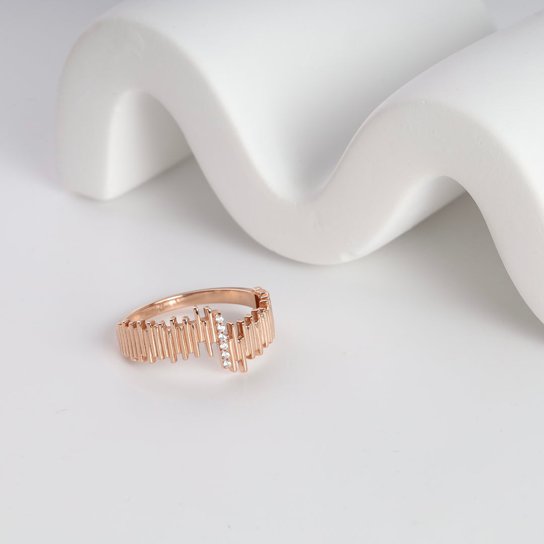 Rose gold geometric ring with vertical bar details and a row of small clear stones, displayed on a white background.