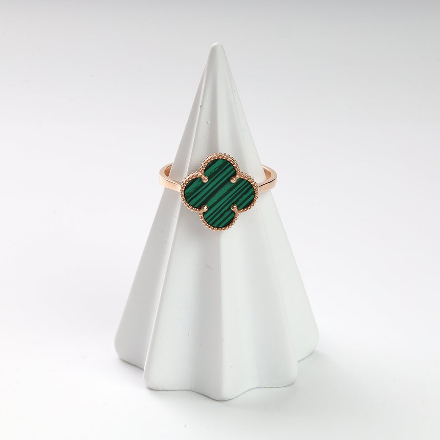 Gold ring with green malachite clover motif displayed on a white ceramic cone, gemstone ring, malachite jewelry.
