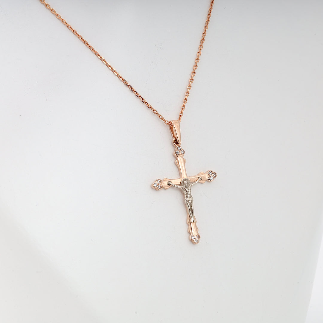 Rose gold crucifix pendant necklace with small clear stones and silver Jesus figure on display, religious jewelry.