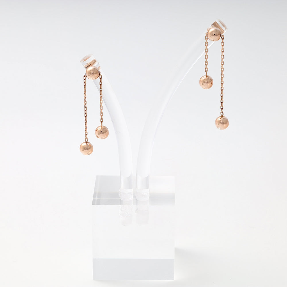 Pair of rose gold drop earrings with two dangling ball charms on each, displayed on a clear stand.