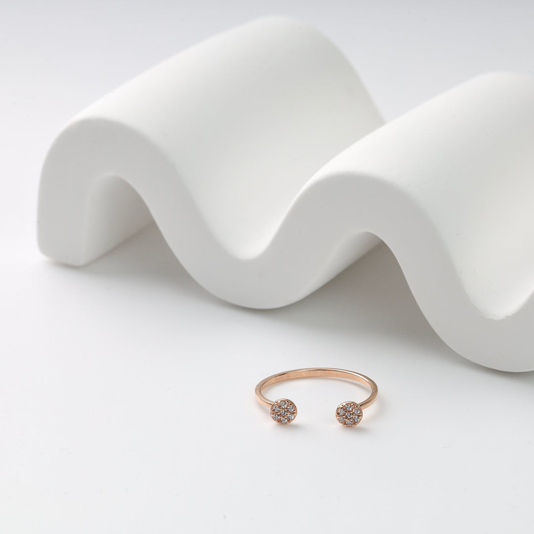 Rose gold open ring with round diamond accents displayed on a white wave-shaped ceramic stand.