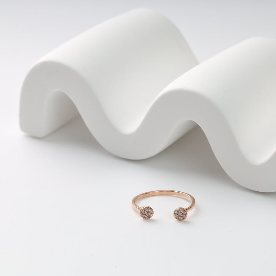 Rose gold open ring with round diamond accents displayed on a white wave-shaped ceramic stand.