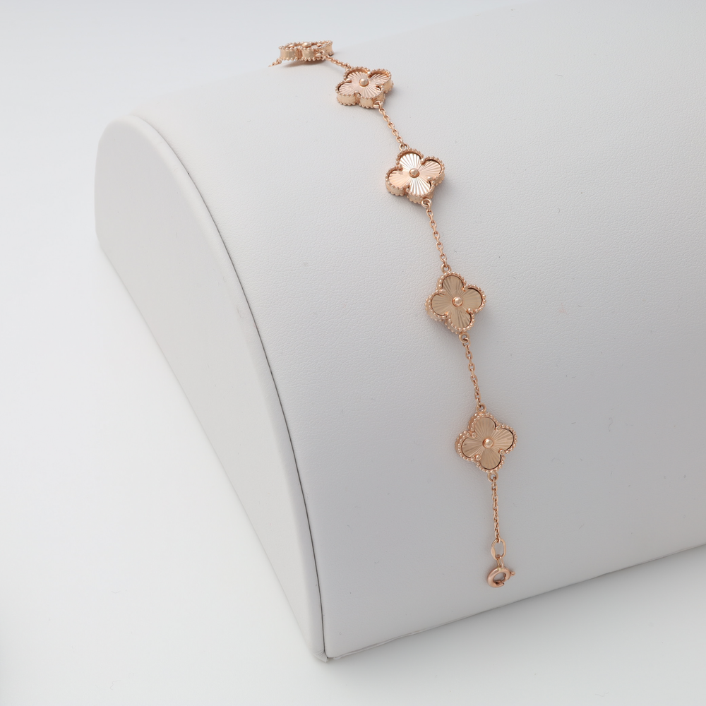Rose gold bracelet with five clover-shaped charms displayed on a white jewelry stand.