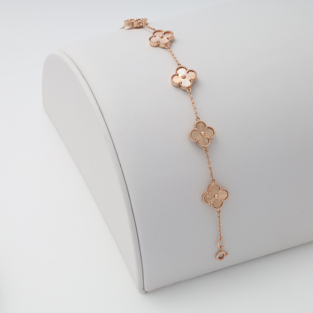 Rose gold bracelet with five clover-shaped charms displayed on a white jewelry stand.