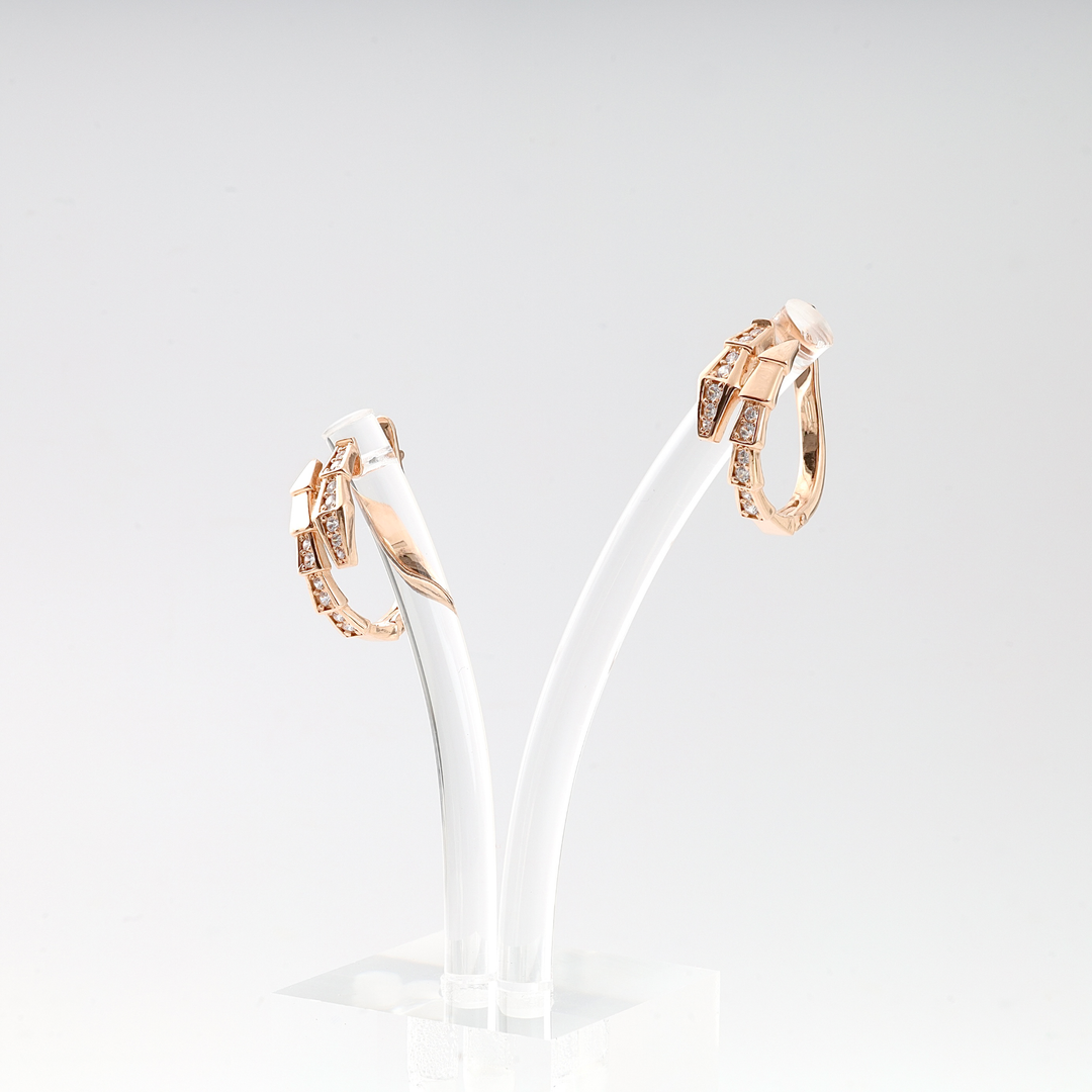 Pair of rose gold hoop earrings with geometric design and clear gemstones displayed on a white stand.