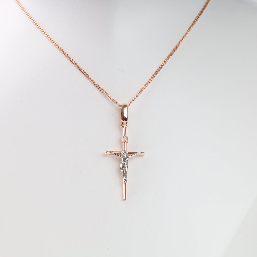 Gold crucifix pendant necklace with silver Jesus figure and a small gemstone on a thin gold chain, displayed against a white background.