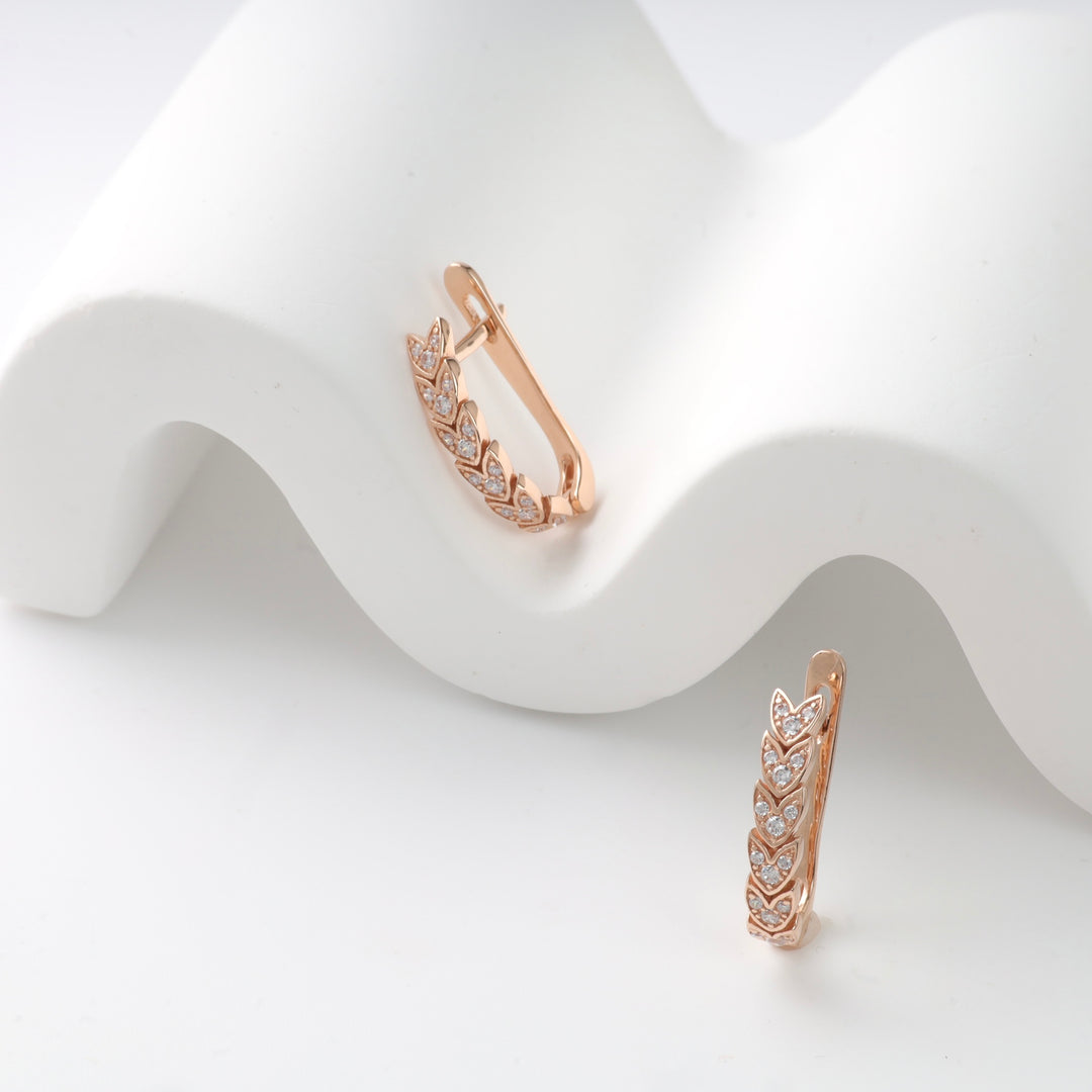Rose gold huggie earrings with leaf and diamond motifs on a white background.