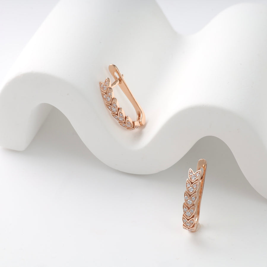 Rose gold huggie earrings with leaf and diamond motifs on a white background.