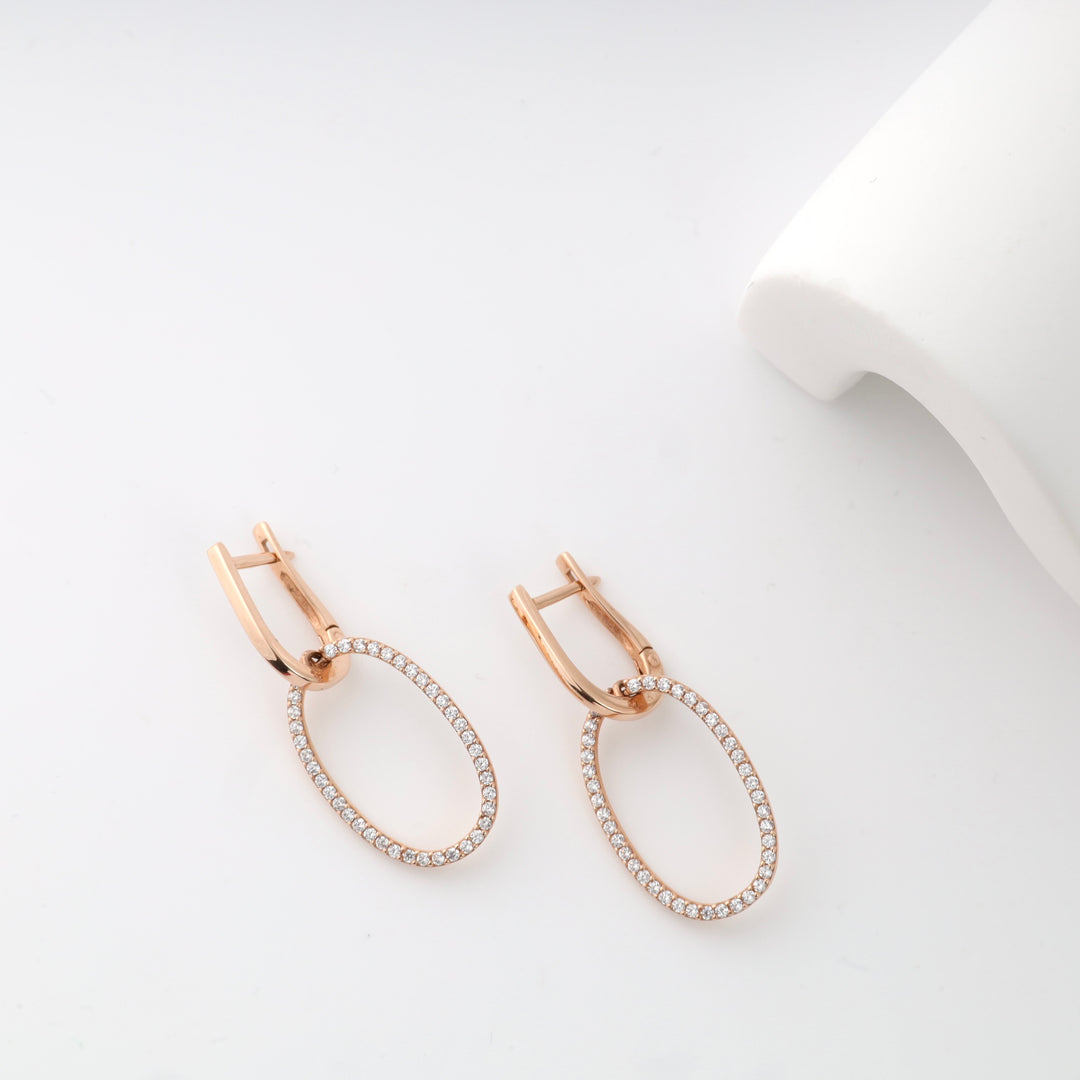 Rose gold hoop earrings with white gemstones on a white background.