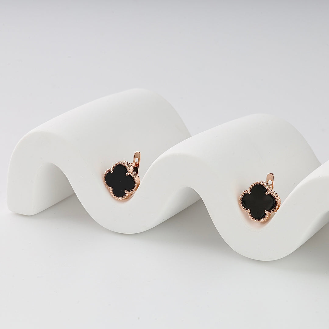 Pair of rose gold clover earrings with black enamel inlay displayed on a wavy white stand, clover drop earrings jewelry.
