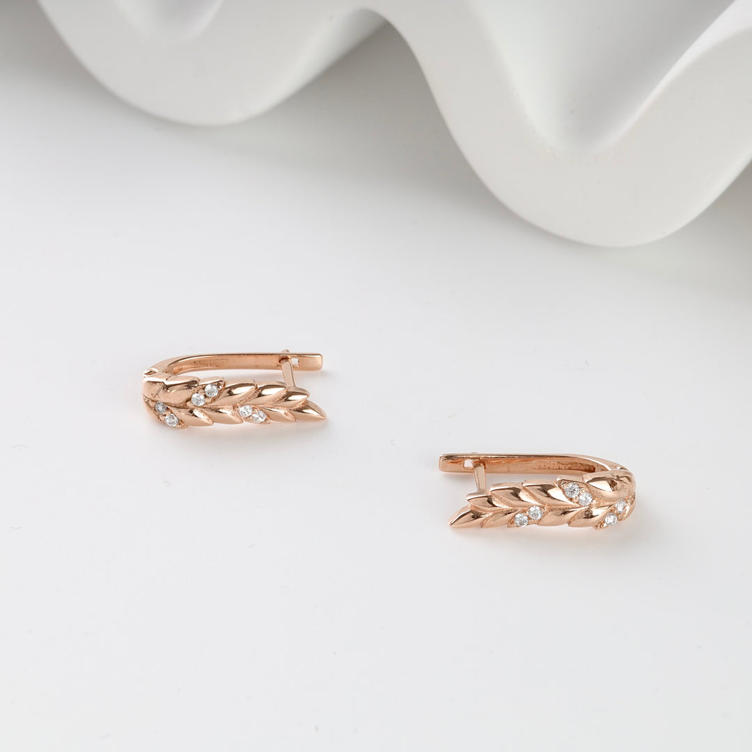 Rose gold hoop earrings with leaf pattern and small clear stones, shown on a white surface.