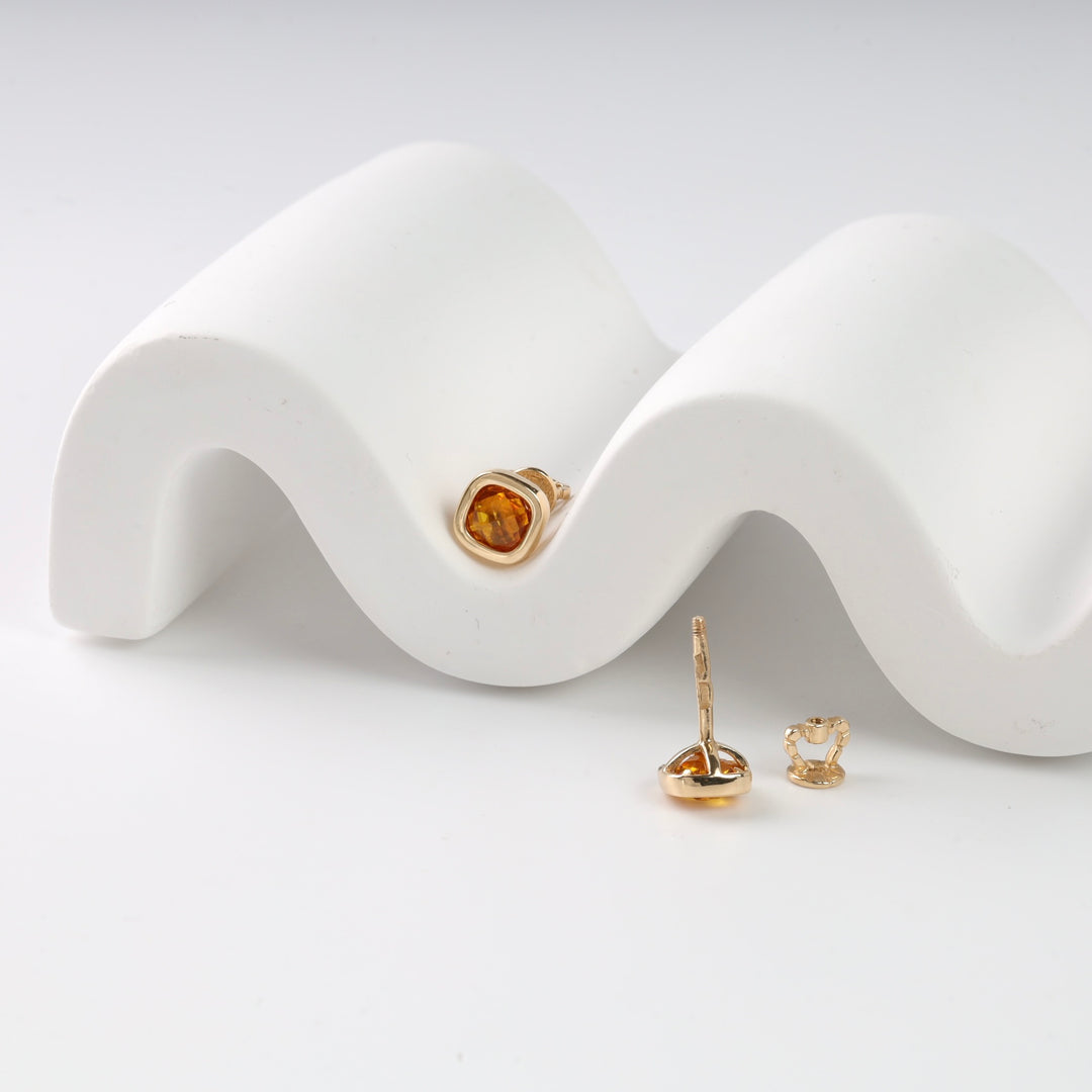 Gold stud earrings with amber stones displayed on a wavy white stand.