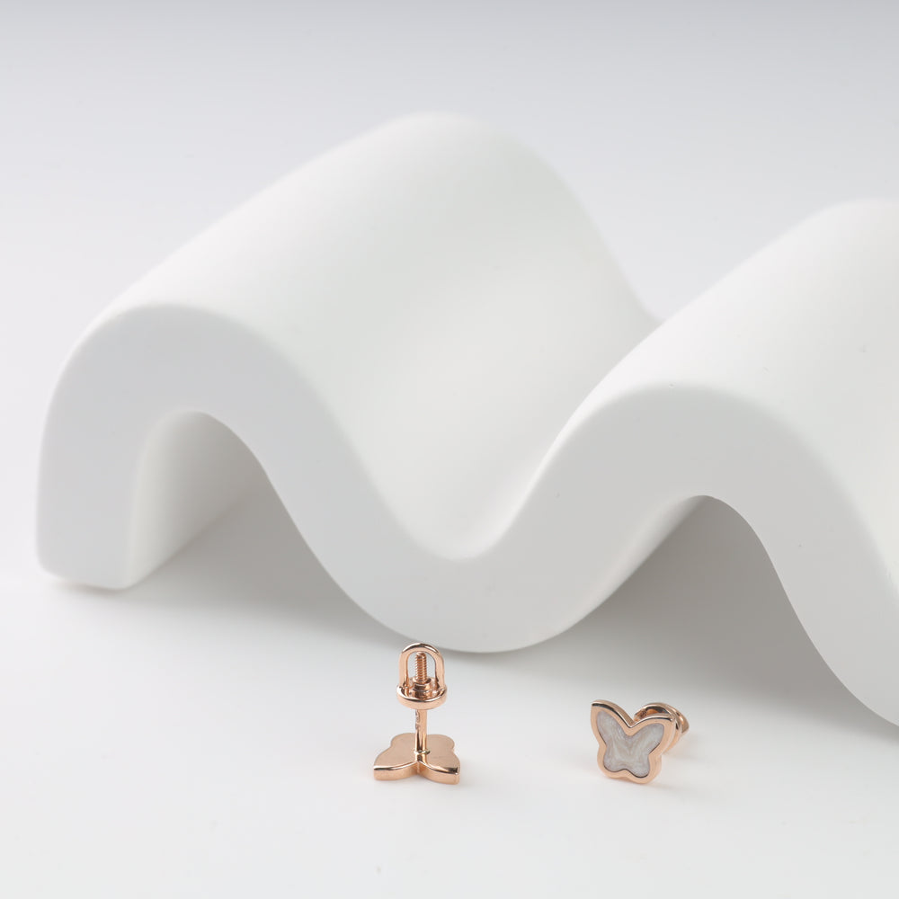 Rose gold butterfly stud earrings with white enamel on white wavy background.