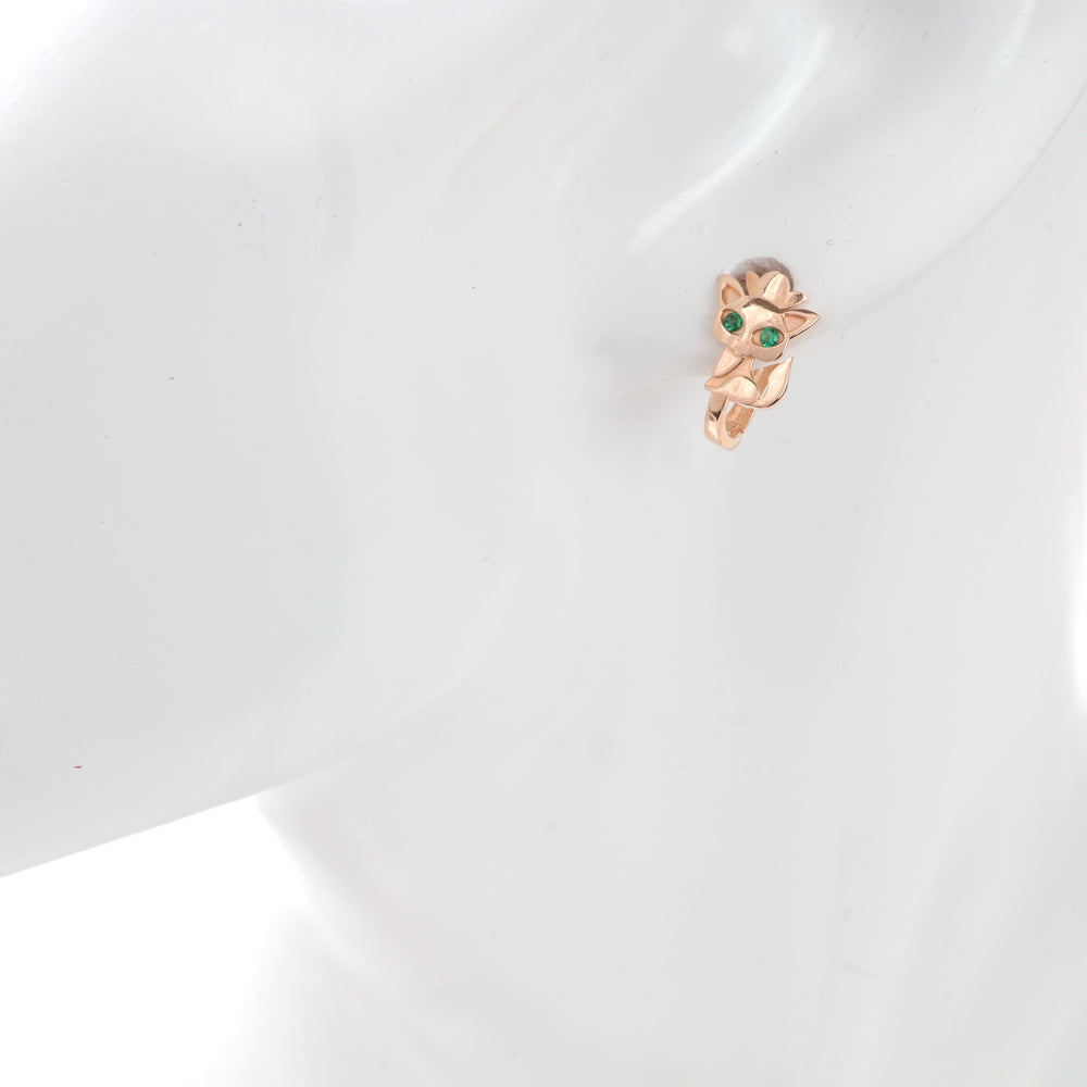 Rose gold owl-shaped huggie earring with green eyes on a white mannequin.