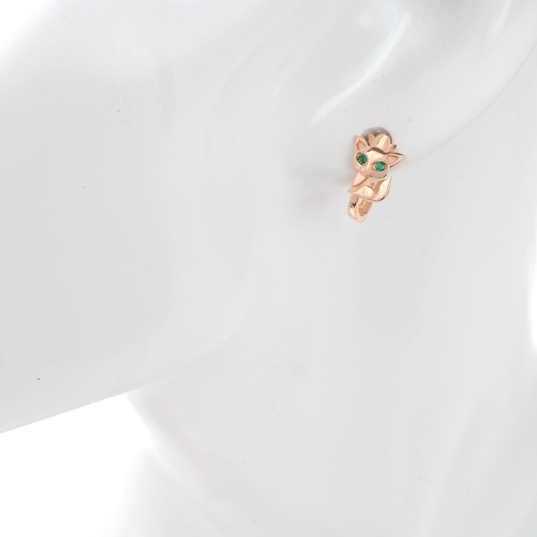 Rose gold owl-shaped huggie earring with green eyes on a white mannequin.