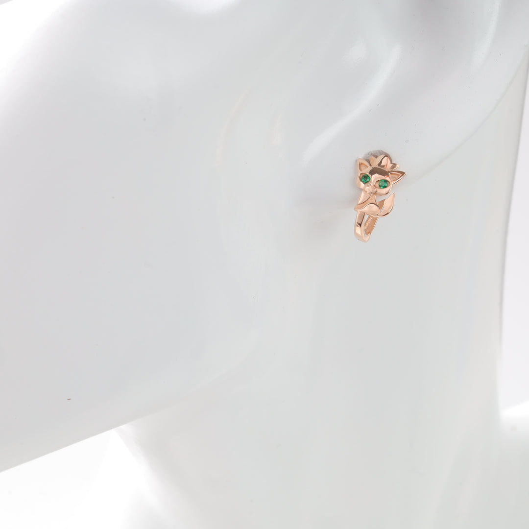 Gold fox-shaped earring with green gemstone eyes on display.