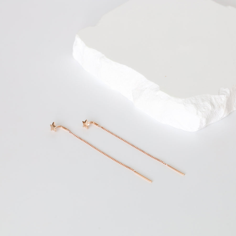 Pair of rose gold star threader earrings with thin bar drops, displayed on a white stone slab.