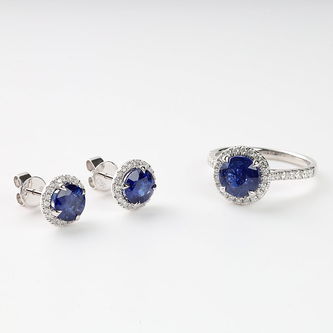 Silver earrings and ring set with round blue sapphire stones and small diamonds displayed on a white background.