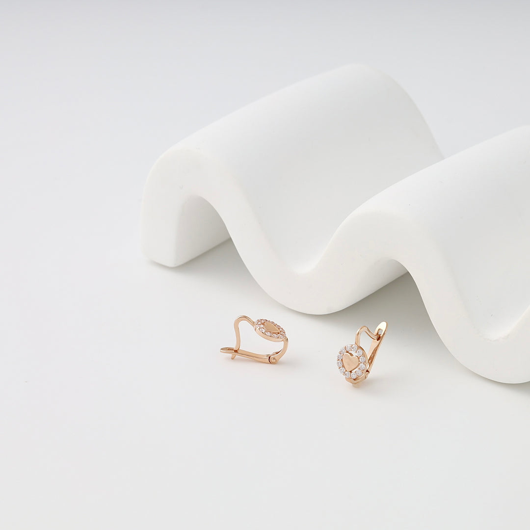 Pair of rose gold oval earrings with clear crystals displayed on a white wavy stand, clip-on earrings jewelry.