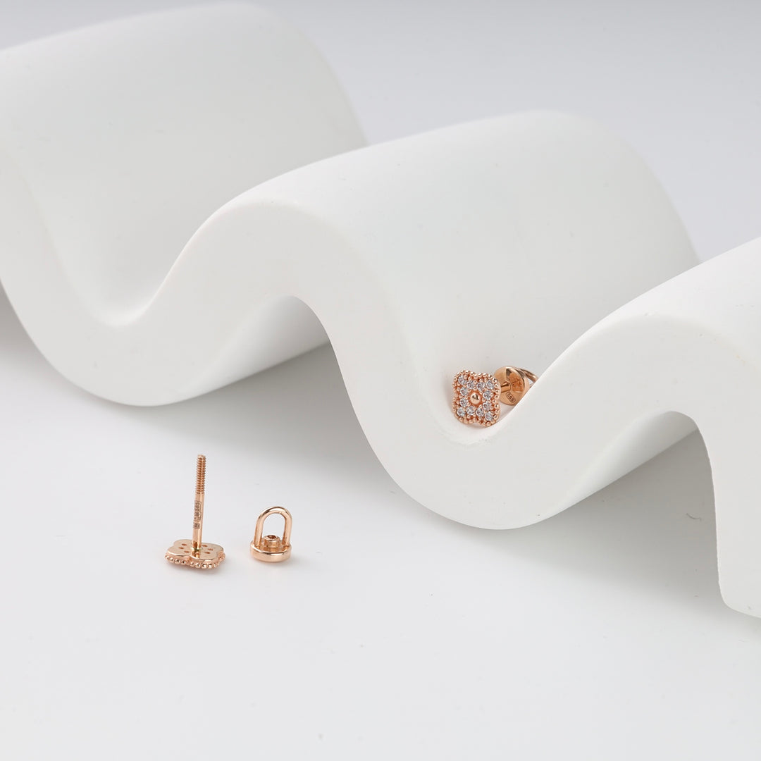 Pair of rose gold square stud earrings with clear pavé stones displayed on a white curved surface, modern jewelry studs.