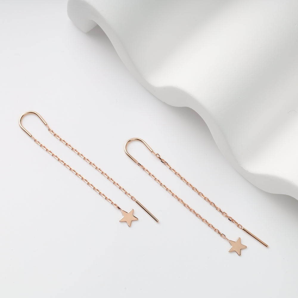 Rose gold chain earrings with star motifs on a white wavy surface.