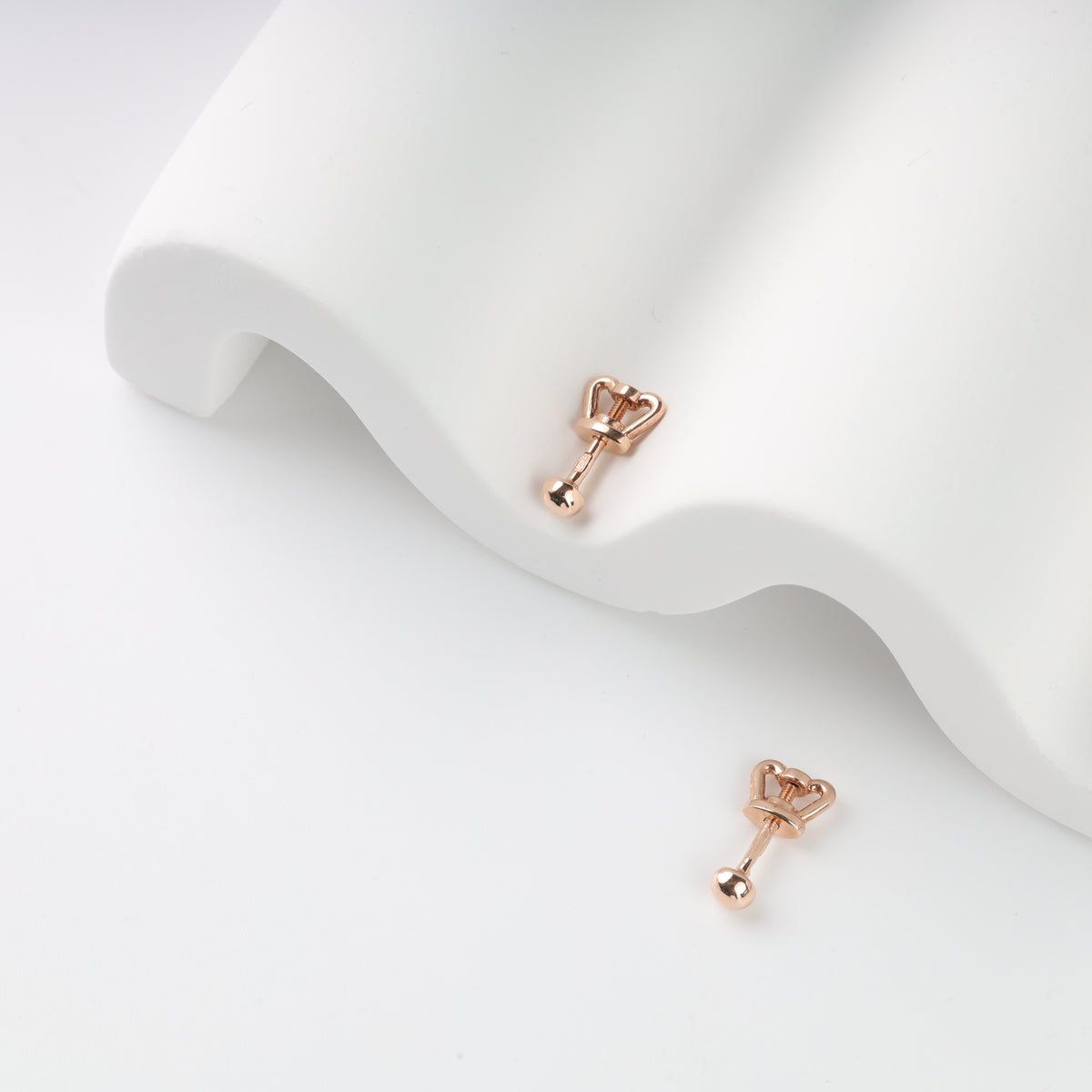 Rose gold arrow-shaped labret piercings on white surface.