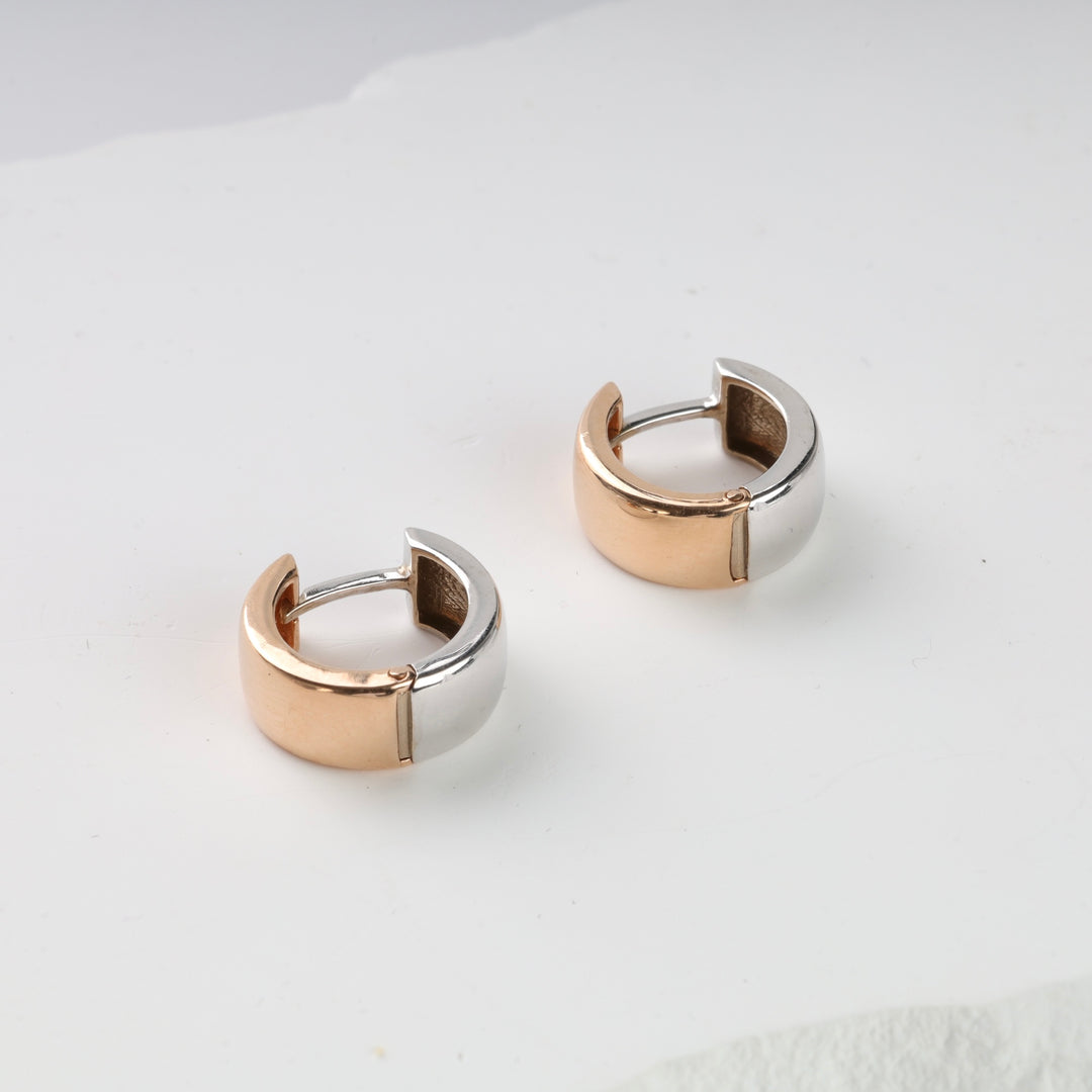 Pair of two-tone huggie hoop earrings in gold and silver metal displayed on a white background.