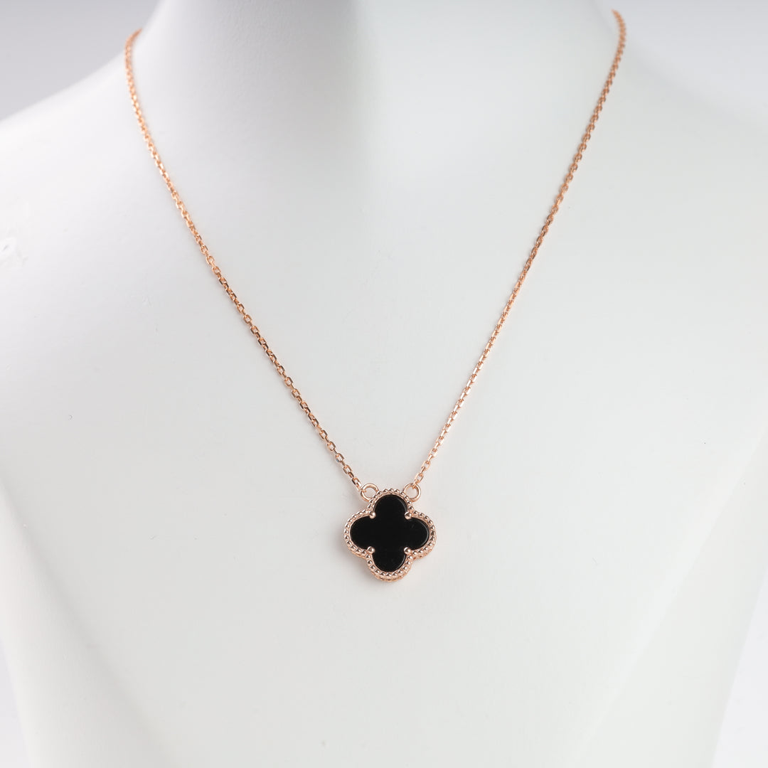 Gold chain necklace with a black clover-shaped pendant displayed on a white mannequin, minimalist jewelry.