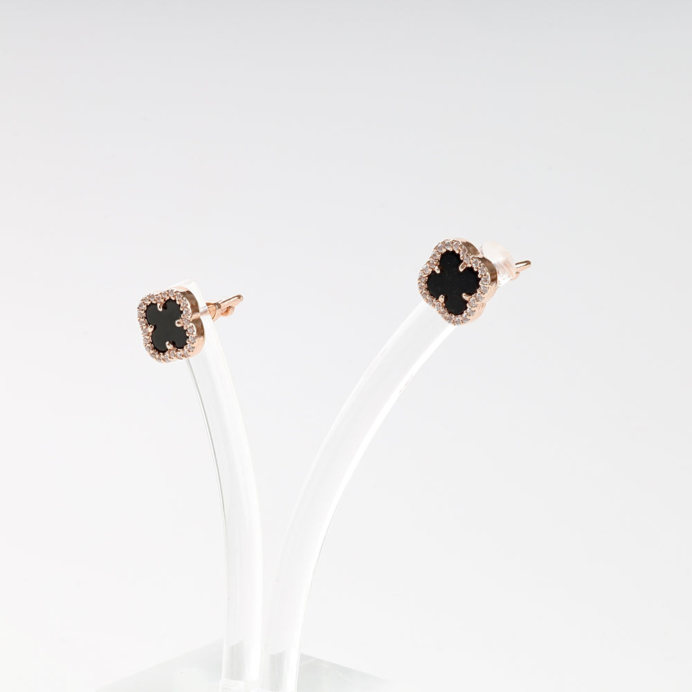 Pair of rose gold stud earrings with black clover-shaped stones and sparkling trim, displayed on a clear stand.