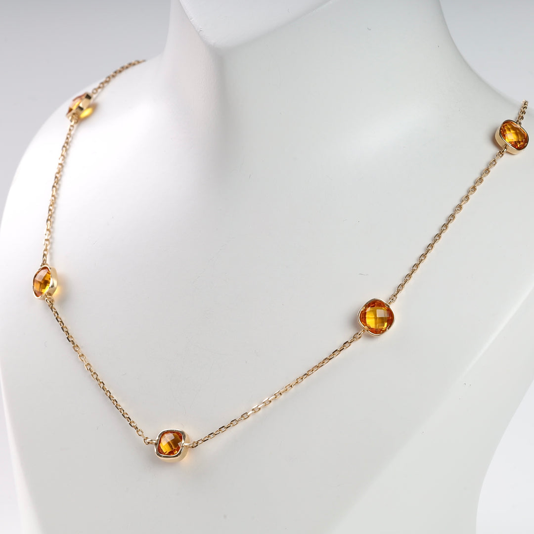 Gold chain necklace with faceted amber stones displayed on a white bust.