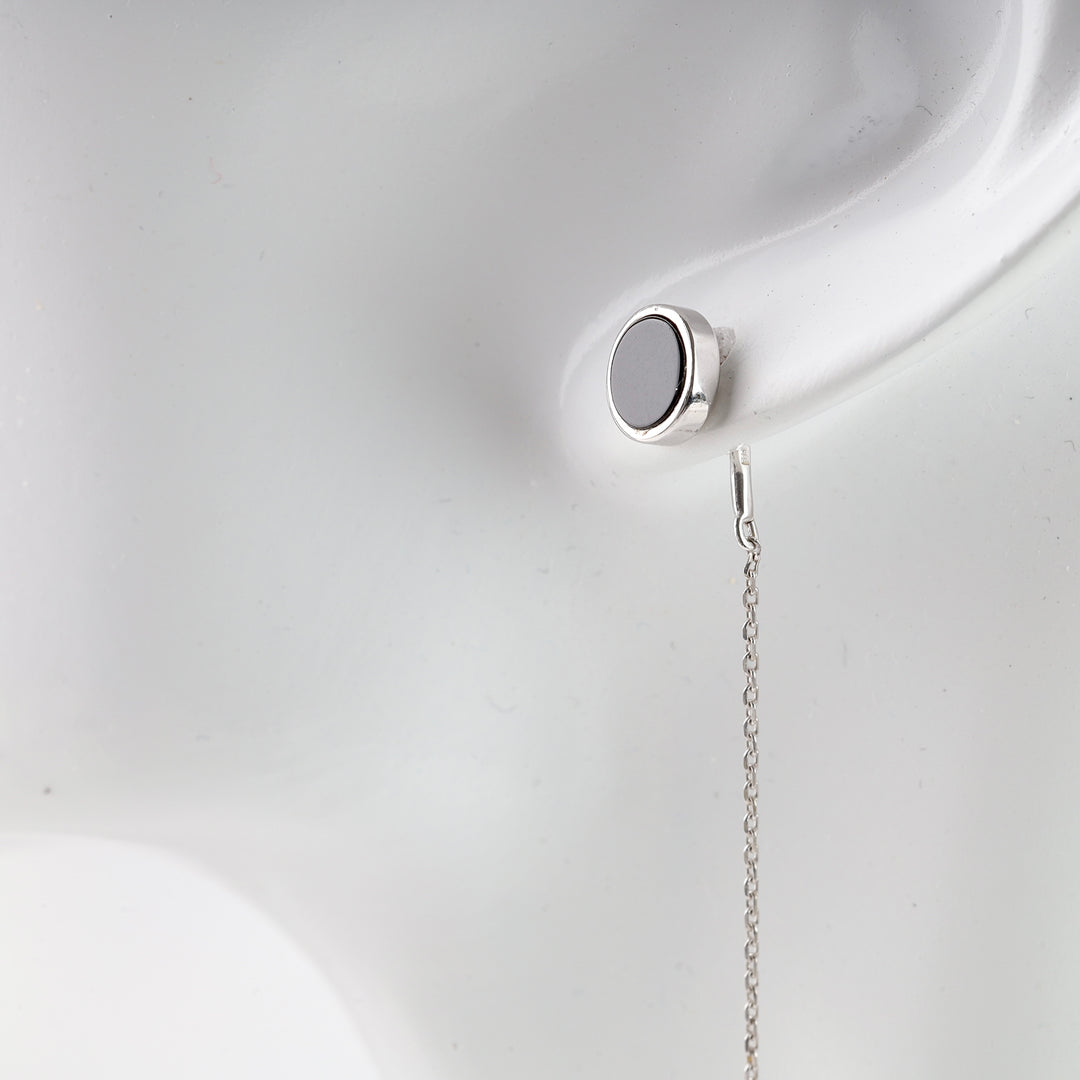 Single silver round stud earring with a black enamel center and fine drop chain displayed on a white mannequin ear.