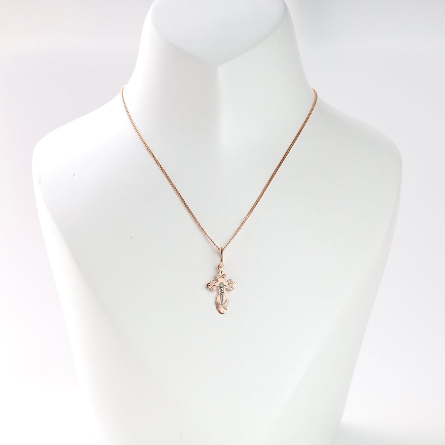 Gold cross pendant necklace with a crucifix motif displayed on a white jewelry bust.