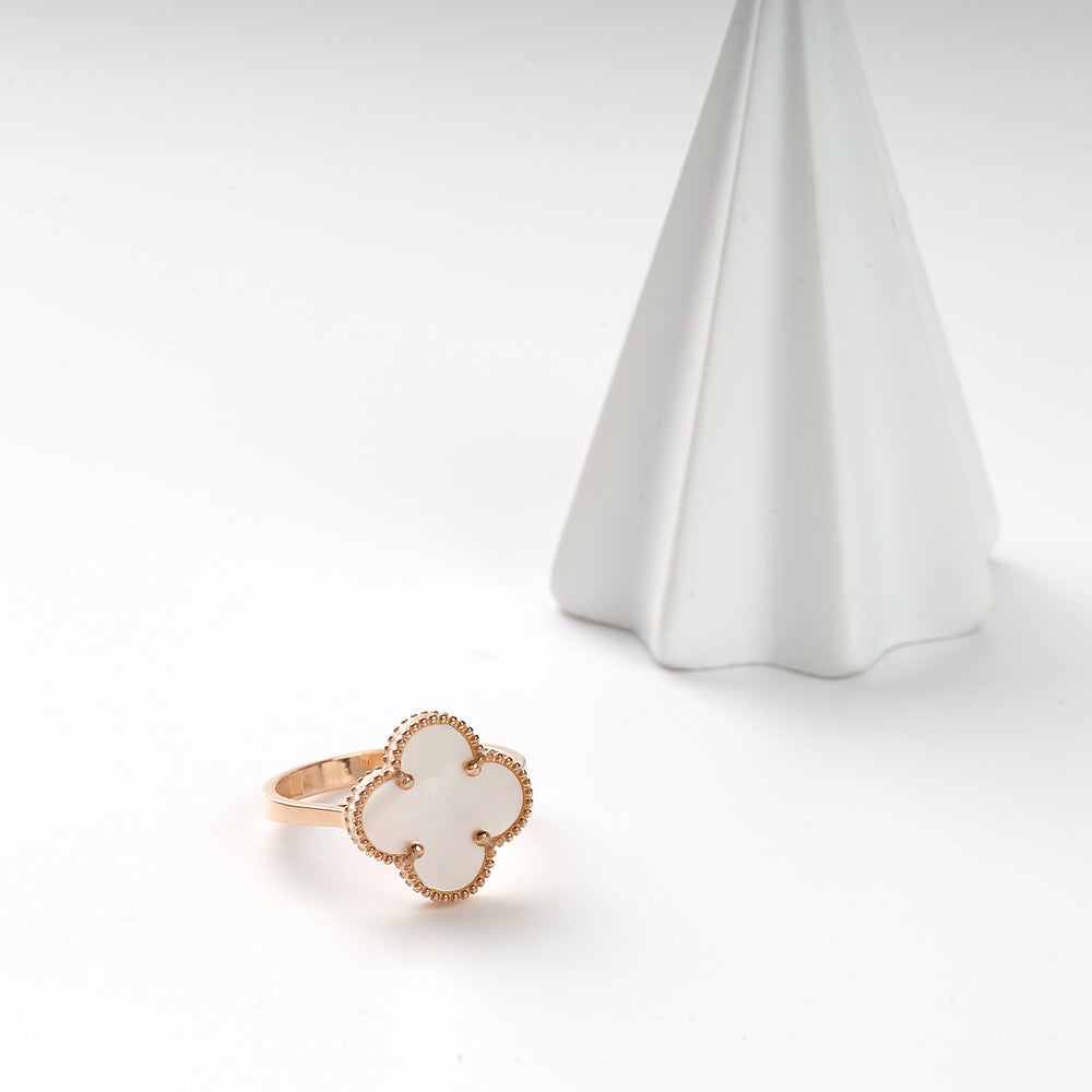 Gold ring with a white quatrefoil motif displayed on a white surface, jewelry, clover ring, minimalist style.