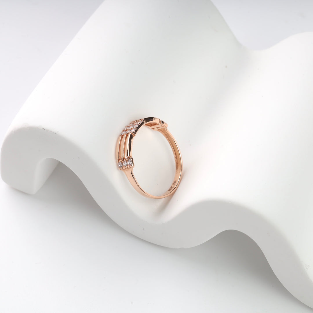 Rose gold ring with cubic zirconia stones on a white wave-shaped display.