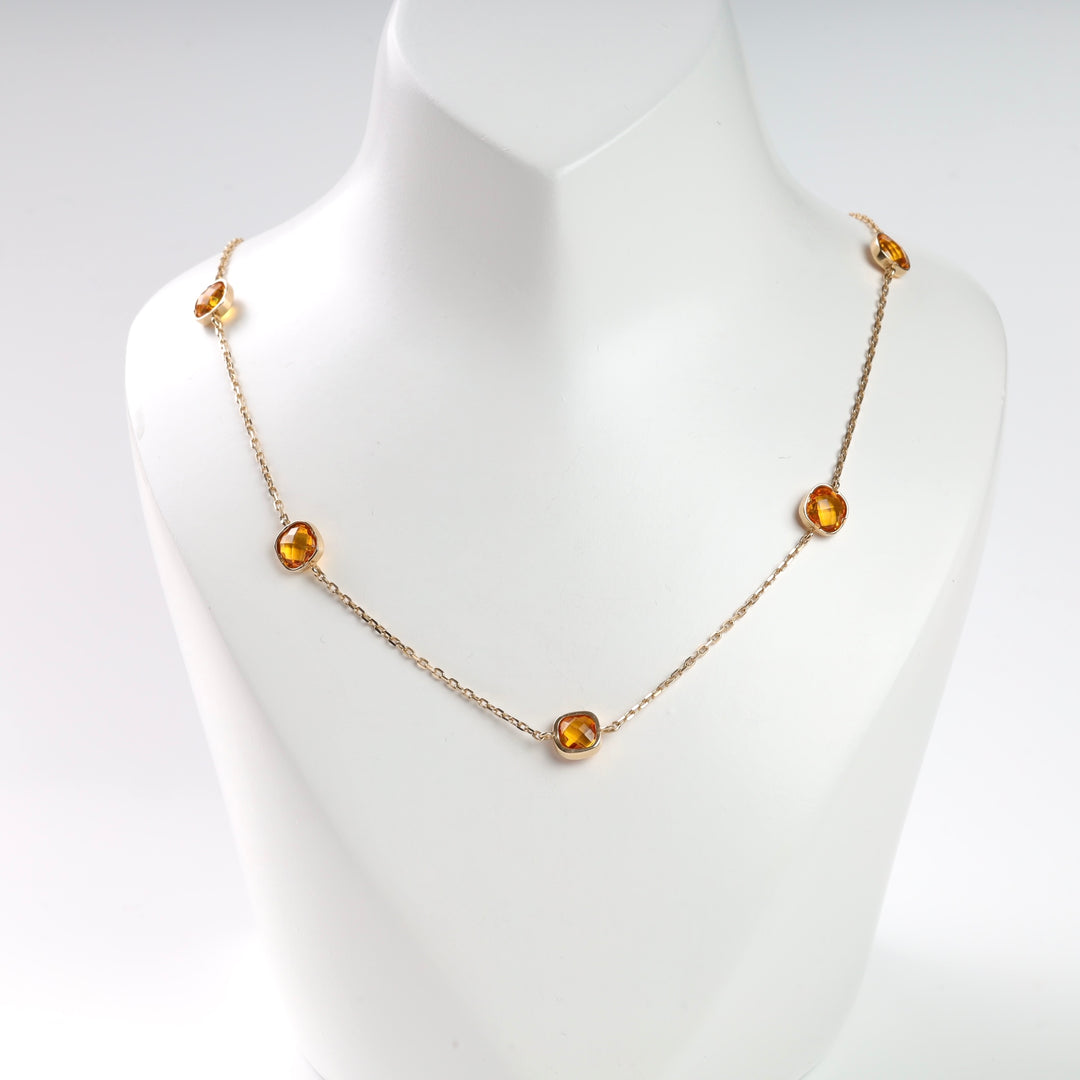 Gold chain necklace with amber gemstones on a white display stand.