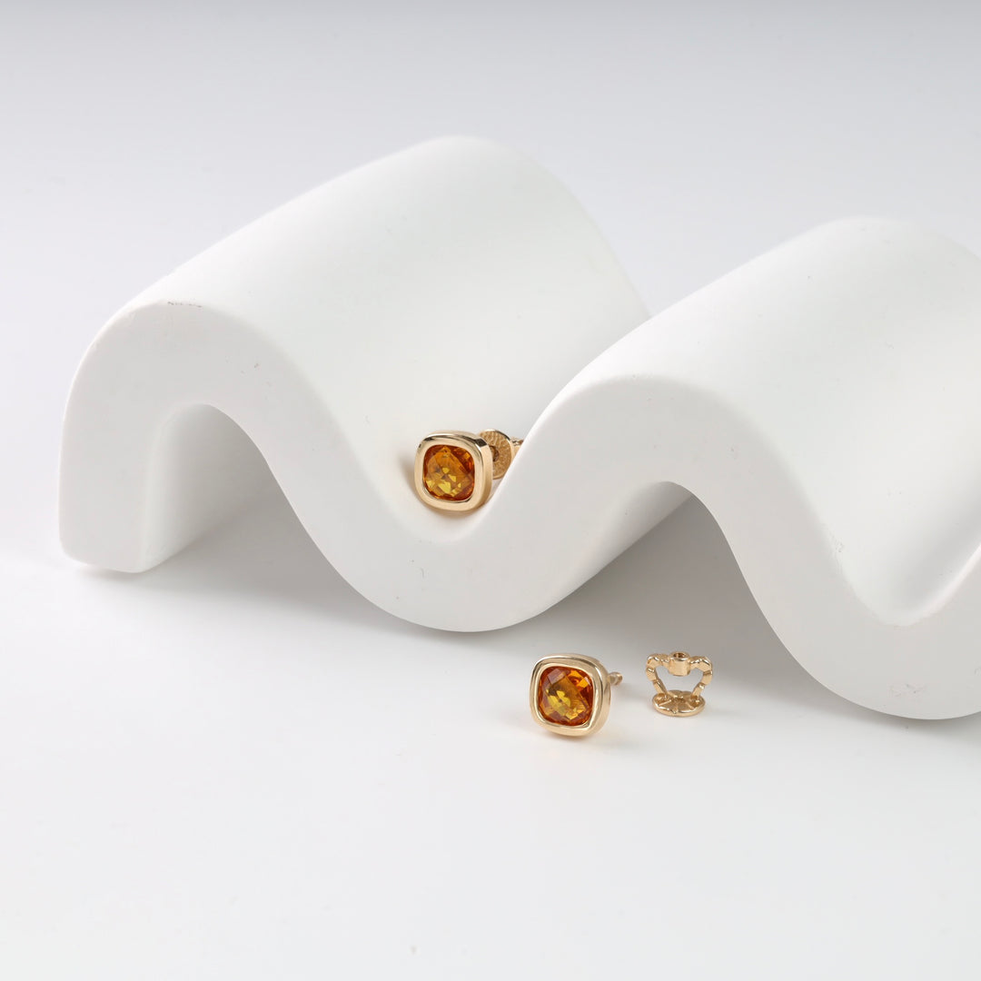 Pair of gold earrings with amber gemstones displayed on a white wavy stand.