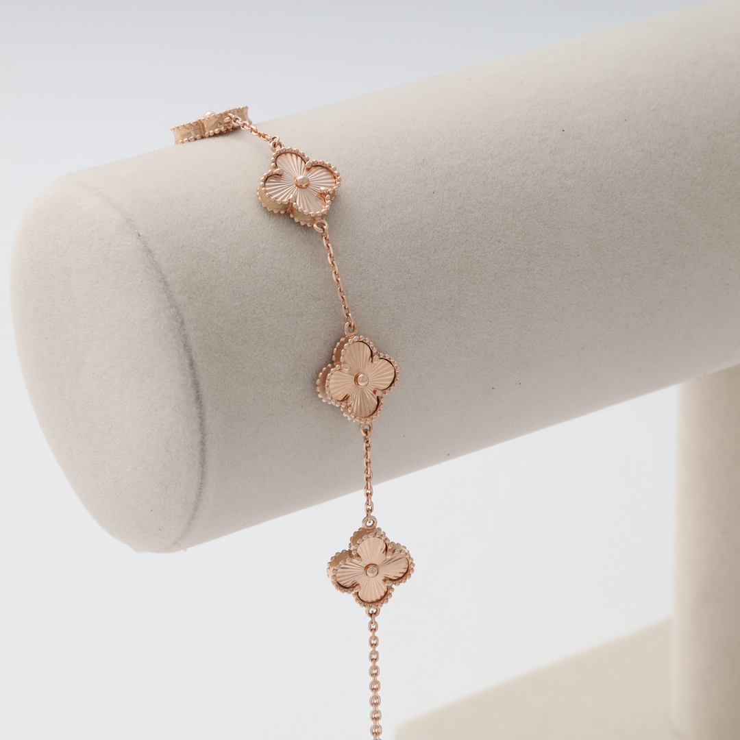 Gold chain bracelet with three four-leaf clover charms displayed on a cream velvet stand.