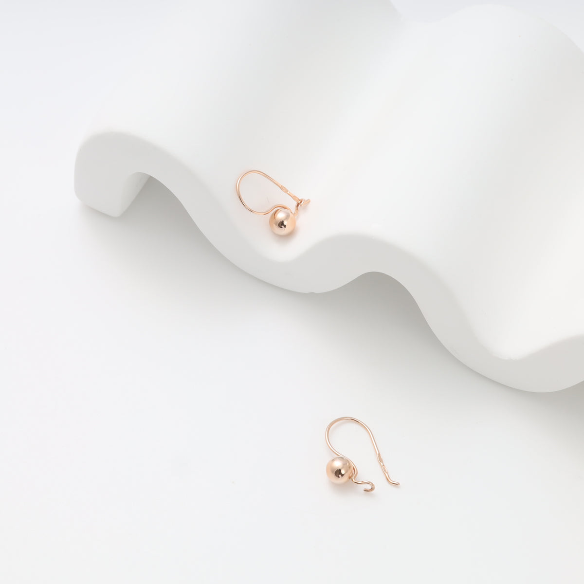 Pair of 14k gold drop ball earrings on white display, minimalist hook dangle Ukrainian Jewelry for everyday gold earrings shoppers.