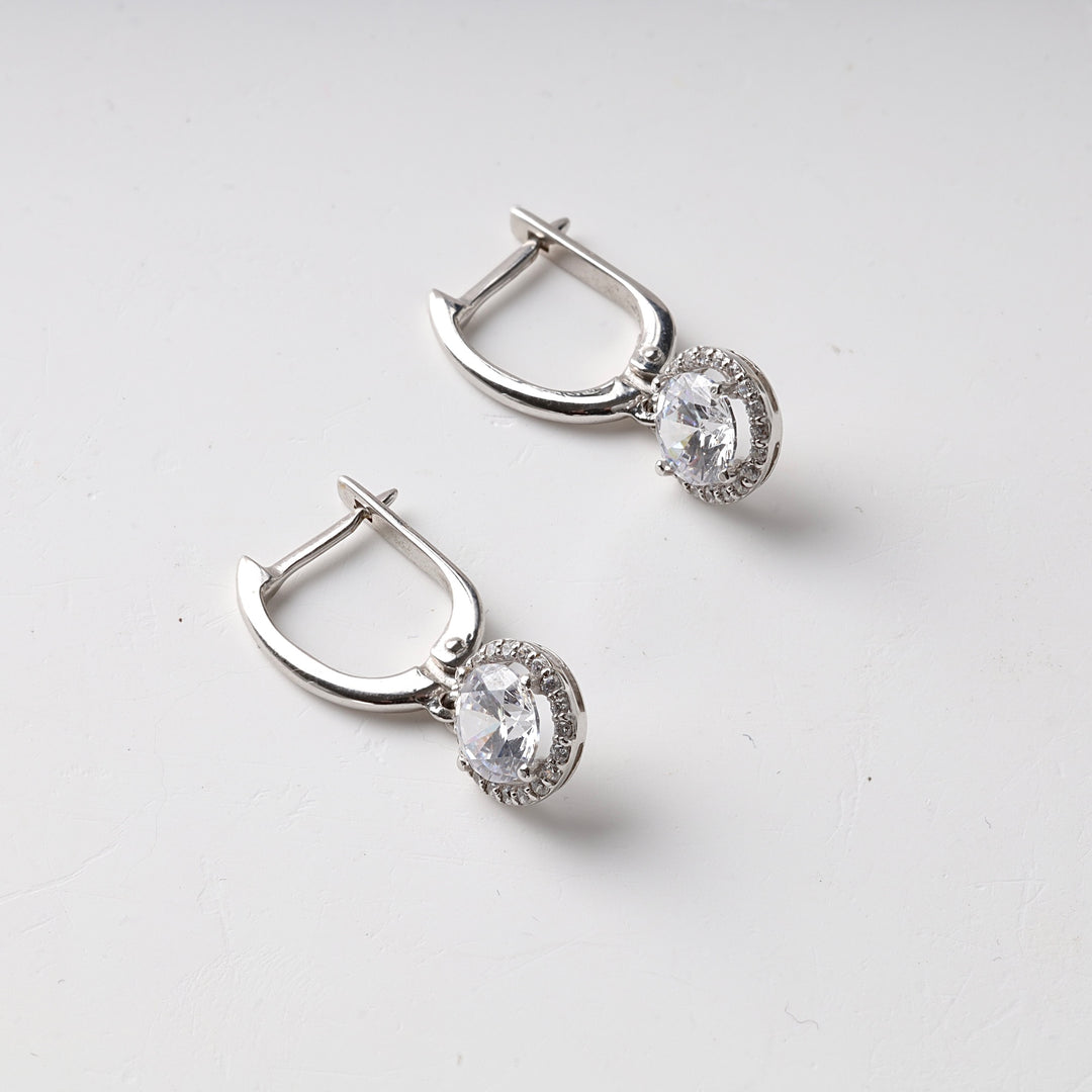 Pair of silver hoop earrings with oval clear stones and small crystal accents displayed on a white background.