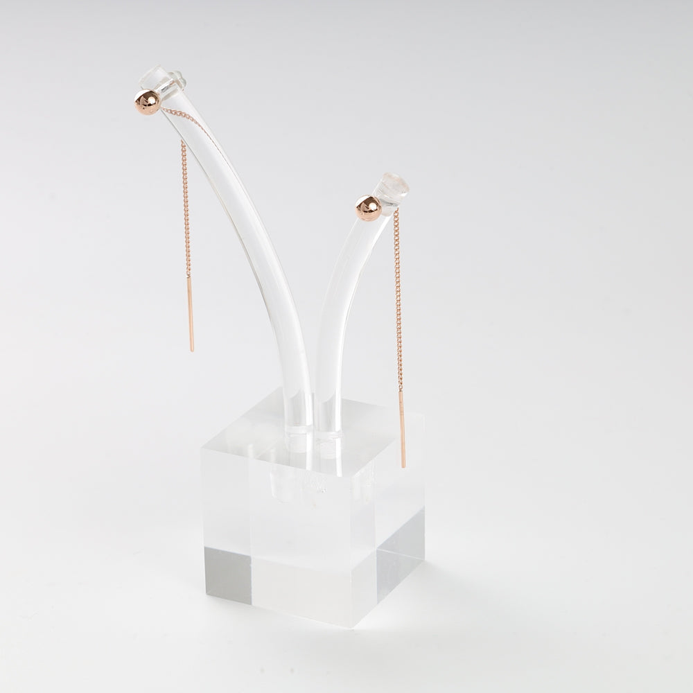 Pair of rose gold threader earrings with ball accents displayed on a clear acrylic stand, minimalist jewelry.