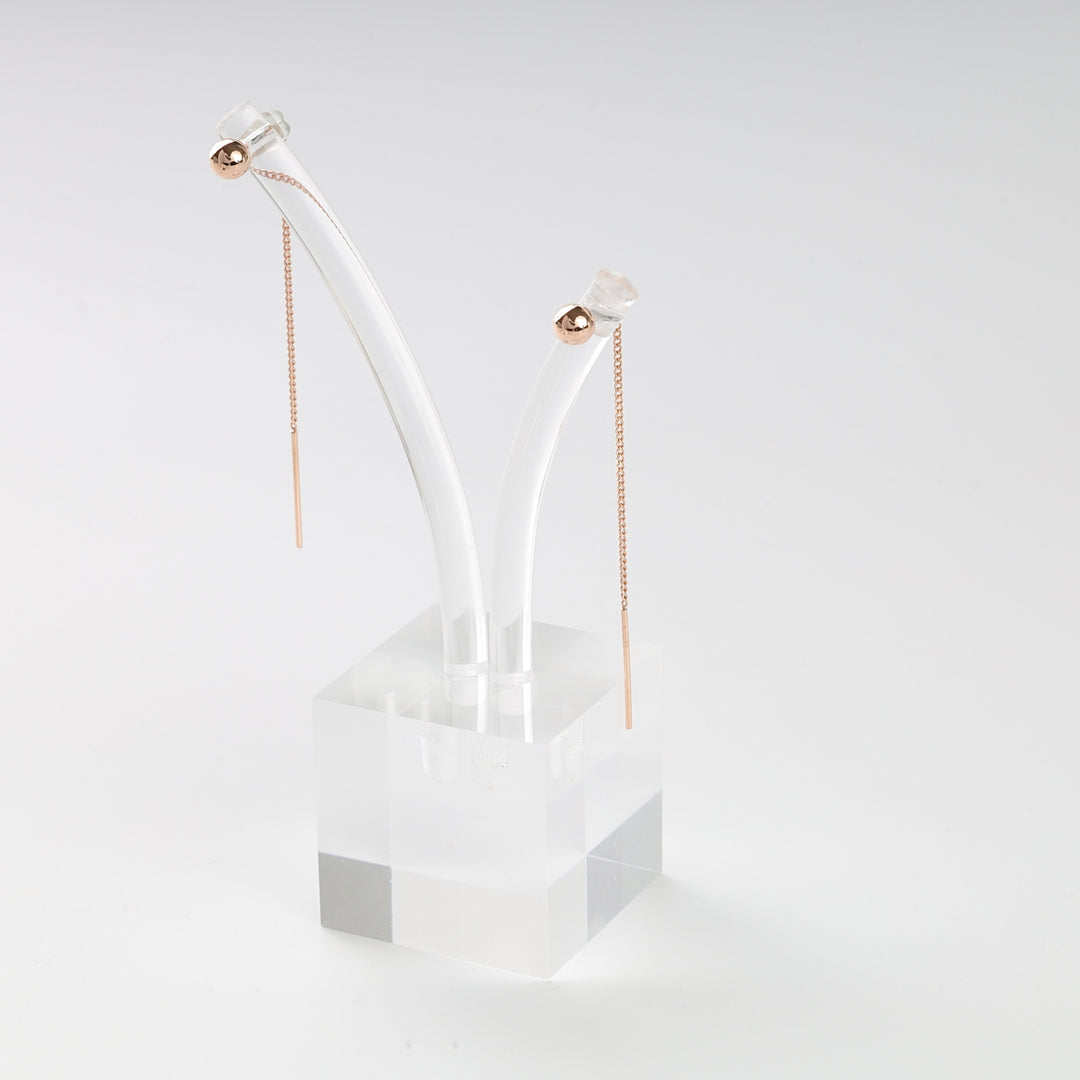 Pair of rose gold threader earrings with ball accents displayed on a clear acrylic stand, minimalist jewelry.