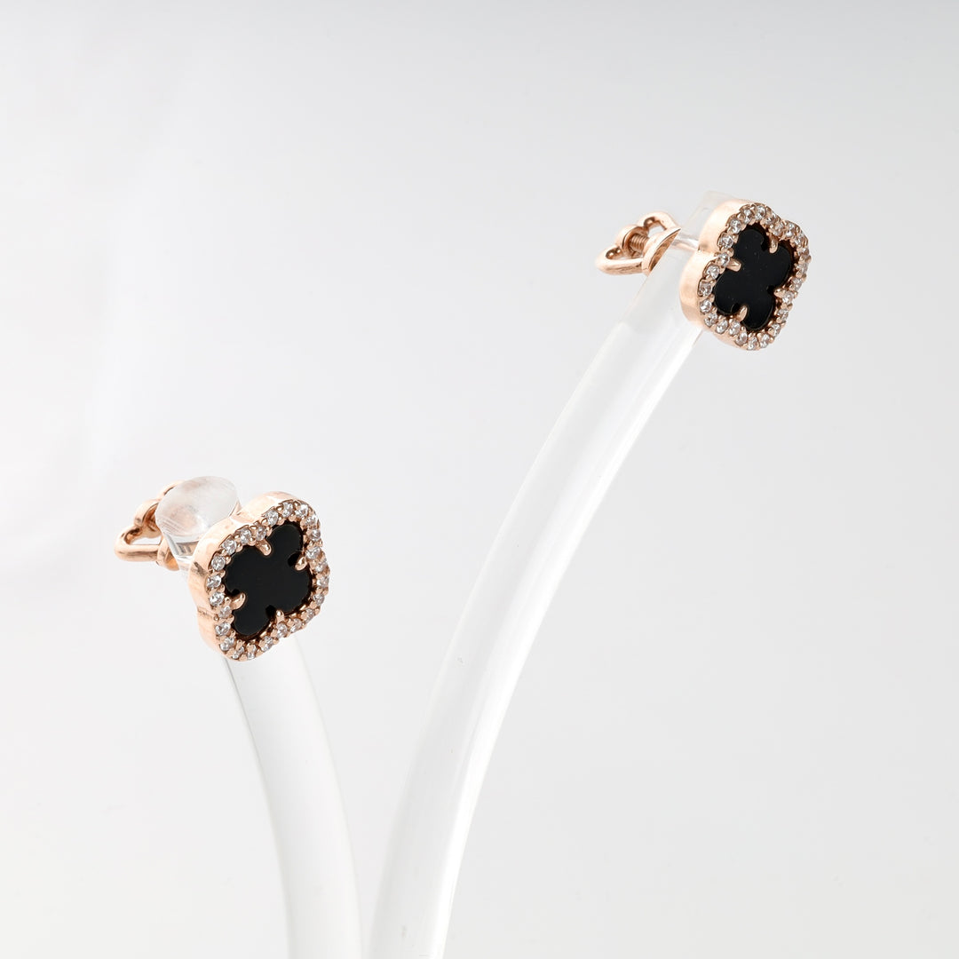 Rose gold clover stud earrings with black onyx center and clear crystals, displayed on a white stand.