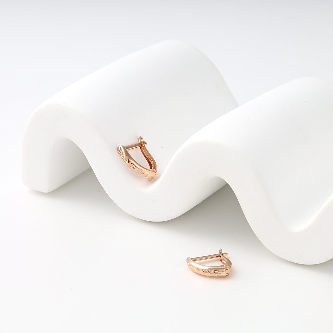 Rose gold 14k gold huggie hoop earrings with engraved pattern on white display, Ukrainian Jewelry for everyday gold earrings shoppers.