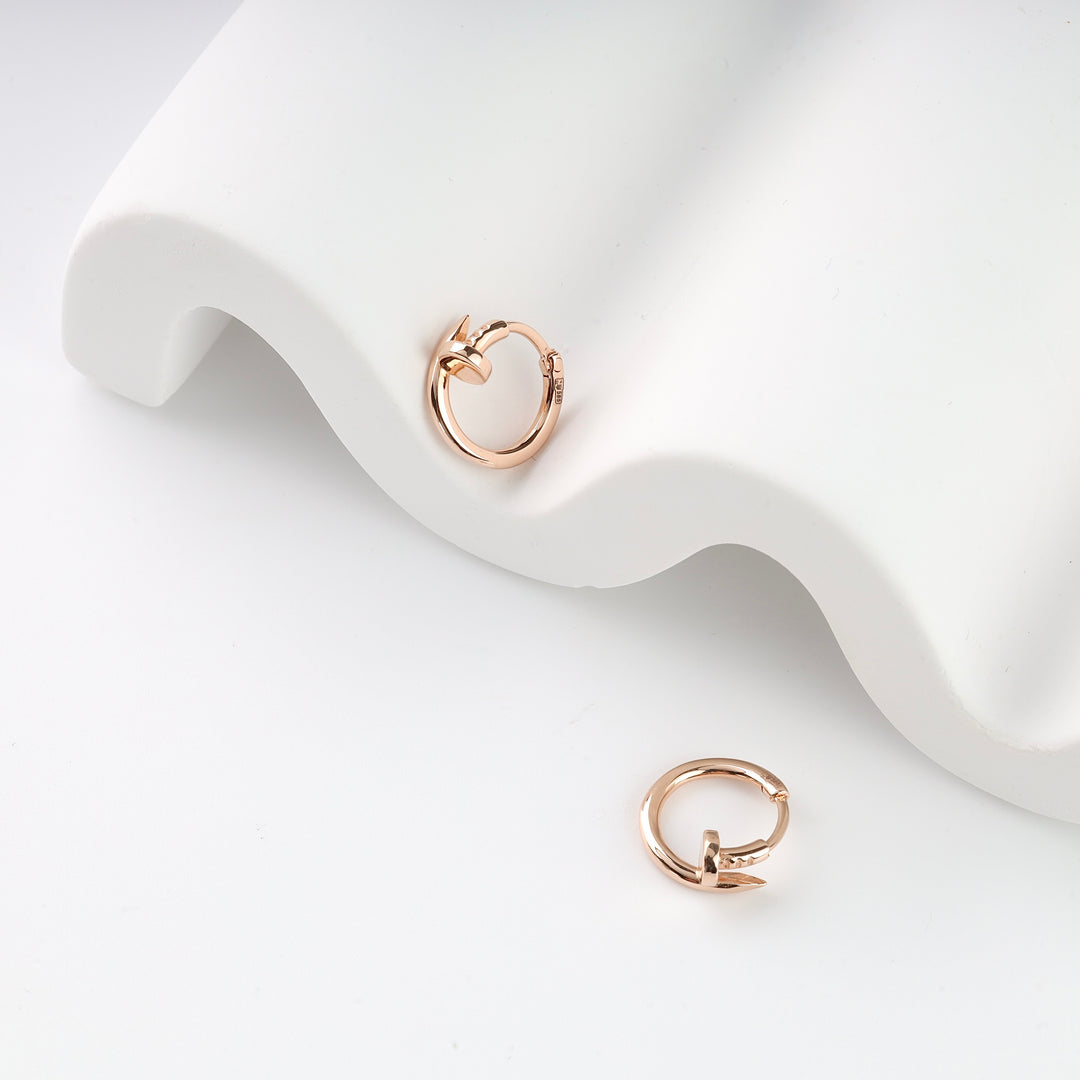 Two rose gold hoop earrings with nailhead design displayed on a white textured surface.