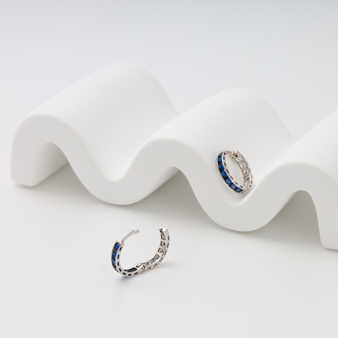 Sterling silver hoop earrings with blue stones, displayed on white waves, Ukrainian Jewelry, silver hoop earrings, sapphire huggies.