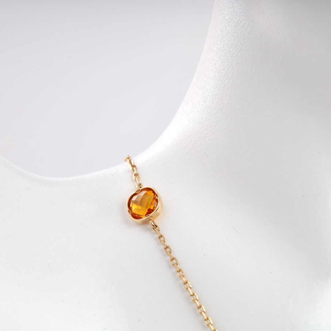 Gold chain necklace with orange gemstone pendant on a white display.