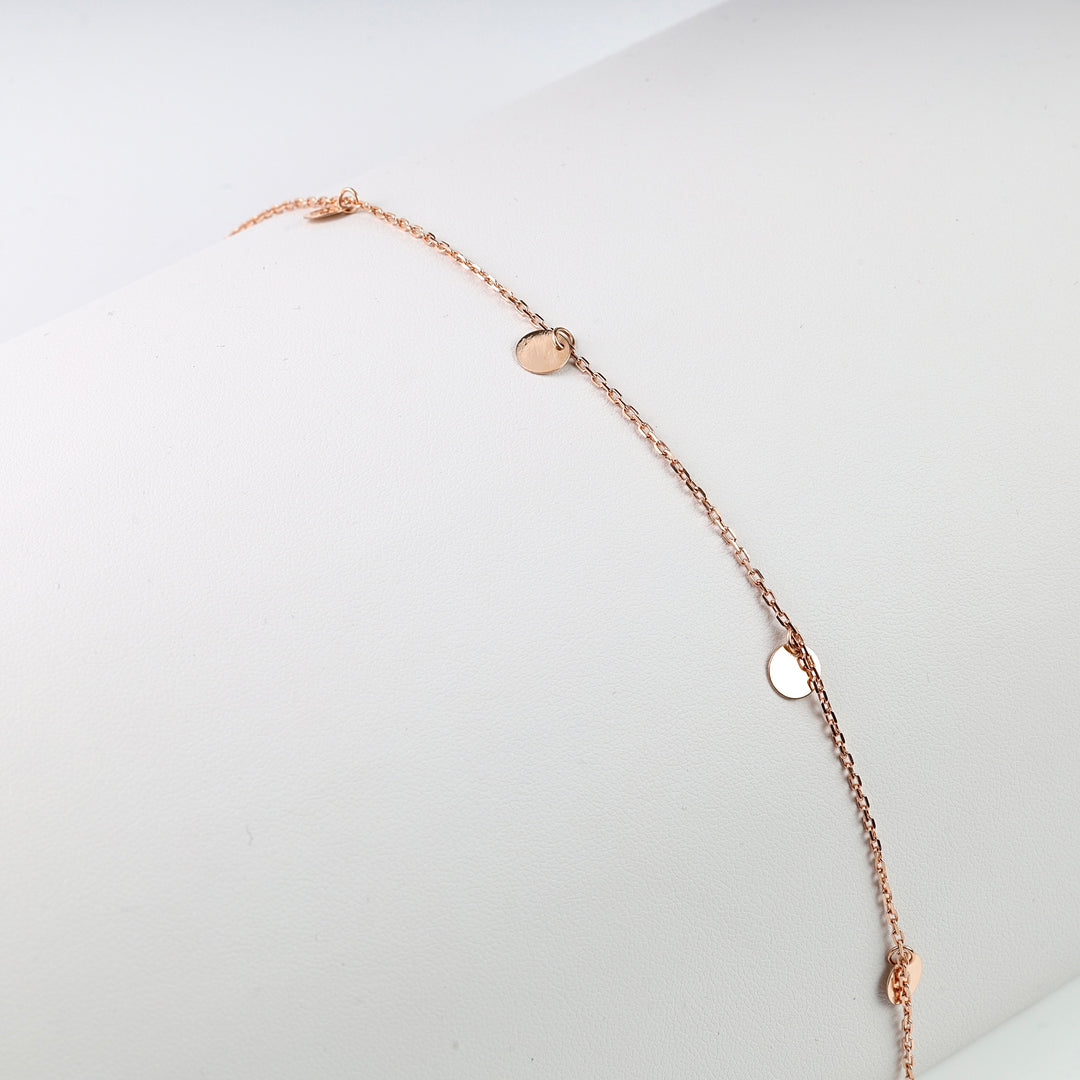 Rose gold chain bracelet with small round disc charms displayed on a white surface.
